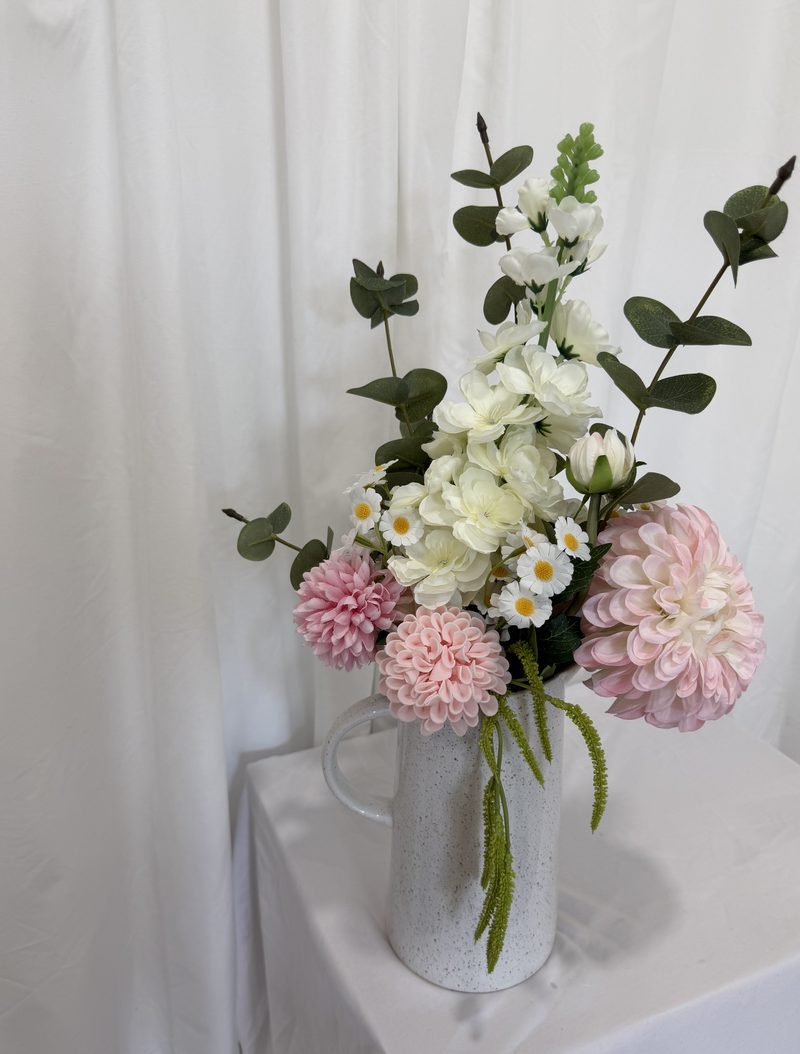 Tall arrangement with upright greenery and blush dahlias in a textured pitcher