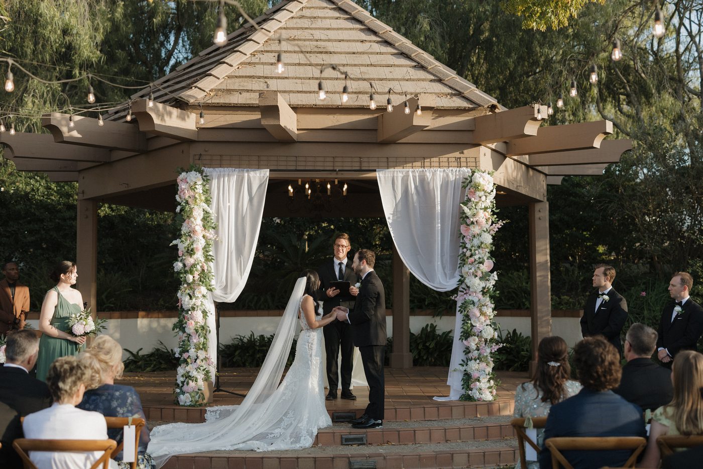 Two large floral installations wrapping the pergola columns at a ceremony