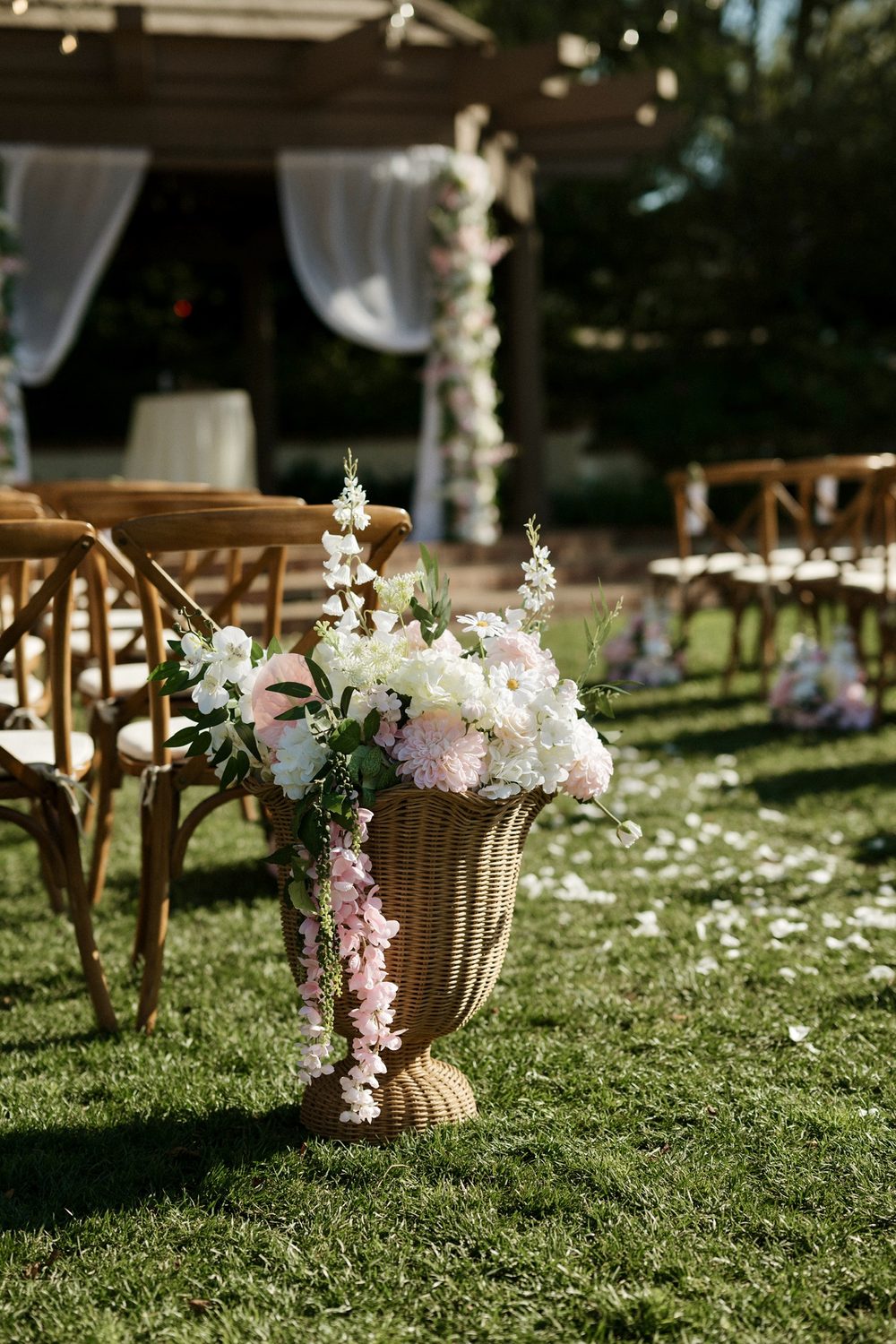 Pedestal arrangement in a woven urn at the end of a ceremony aisle