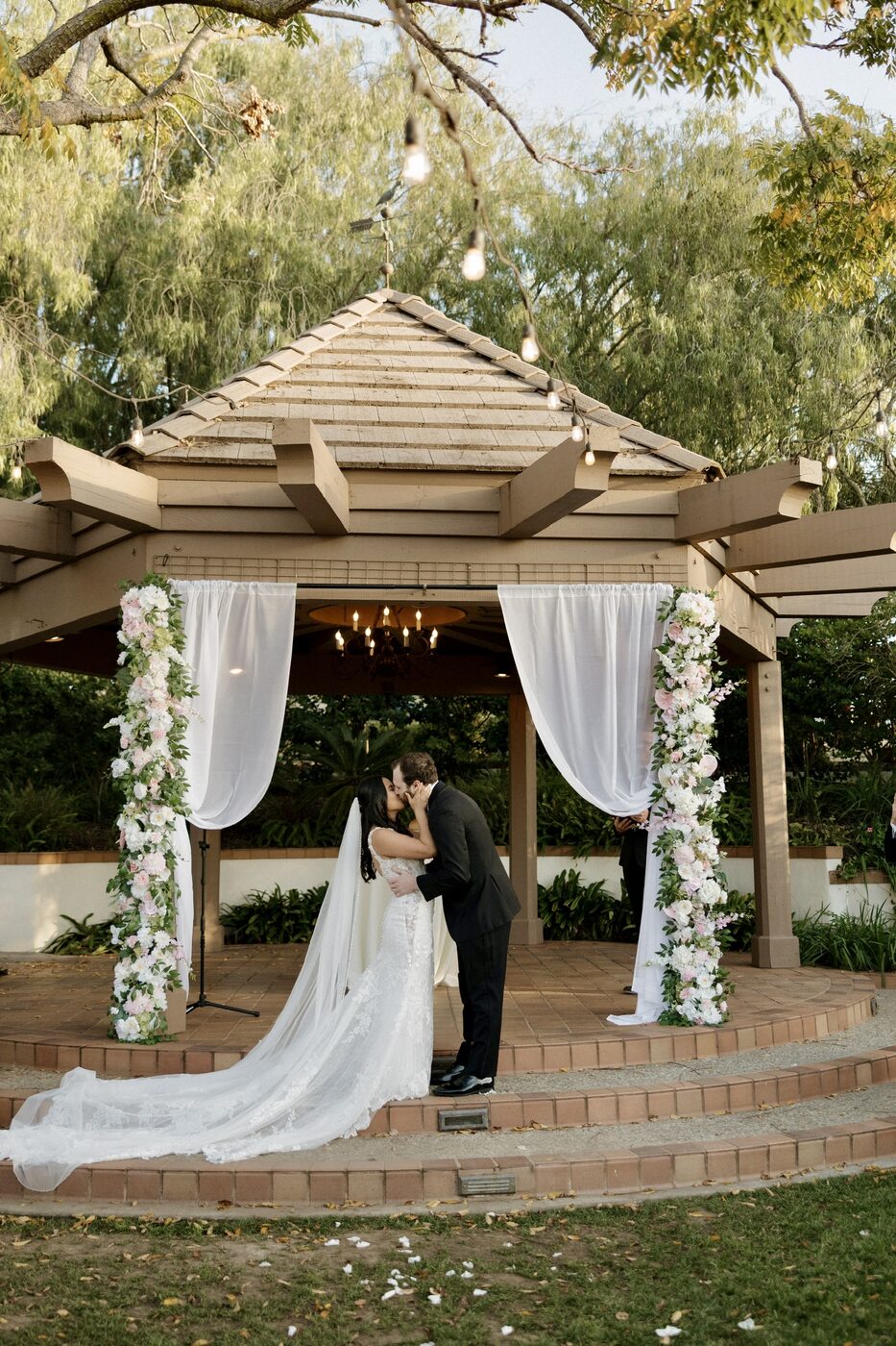 Couple sharing their first kiss under a floral-draped gazebo